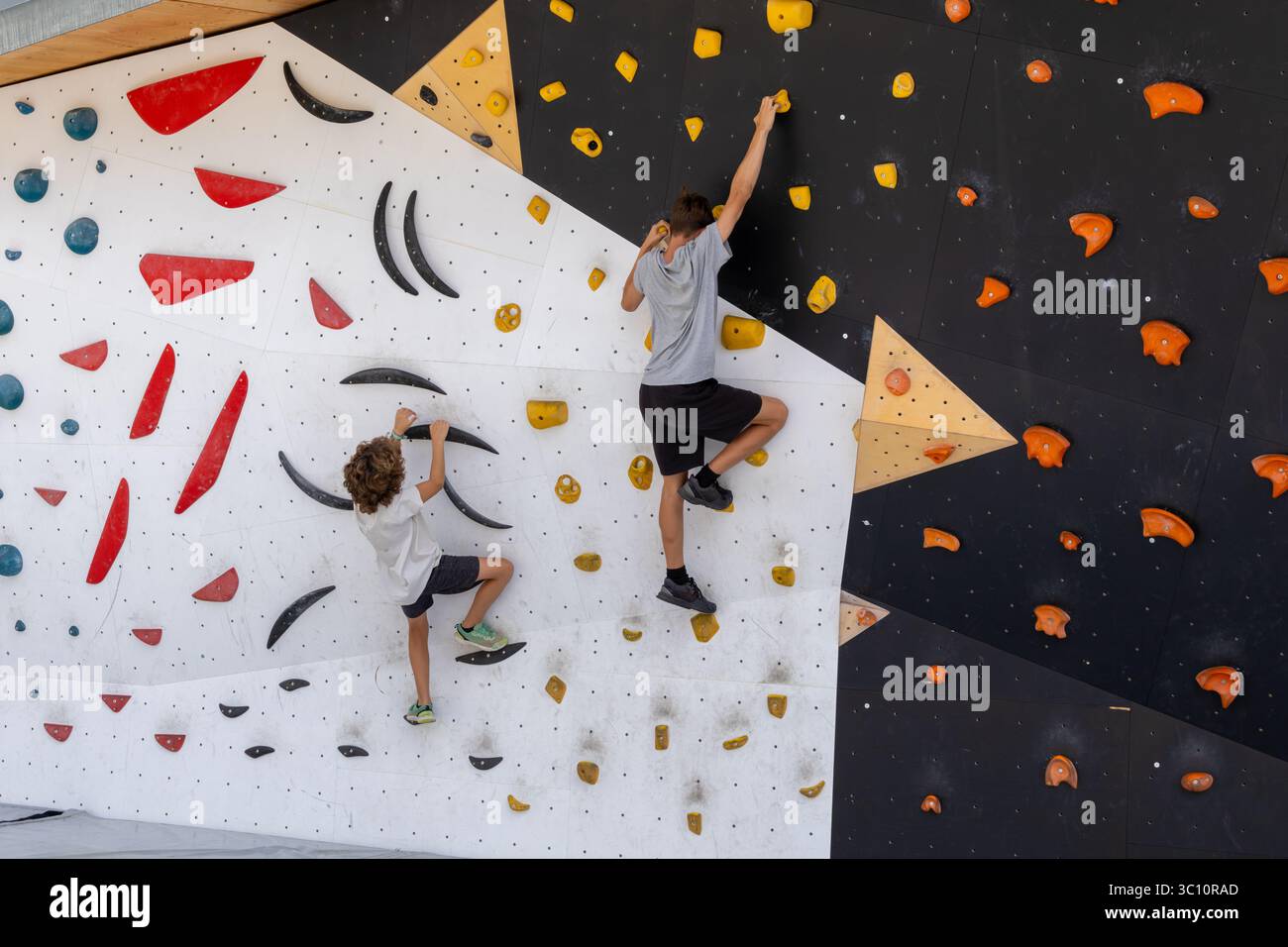 Due bambini che si arrampicano su una parete di roccia artificiale, si divertono ad attività fisica e sviluppano abilità di arrampicata in un ambiente sicuro e controllato Foto Stock