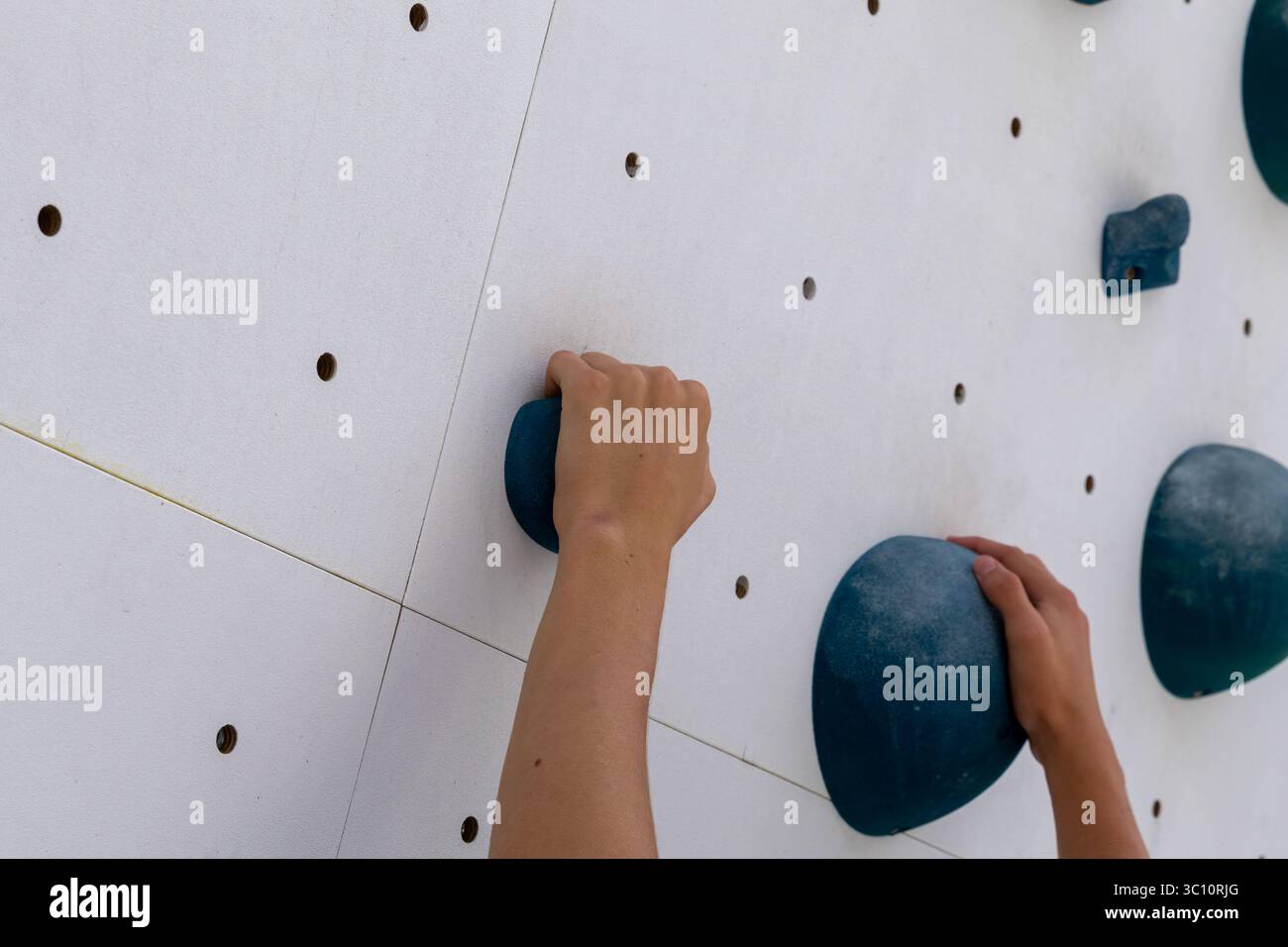 Le mani del bambino afferrano una parete bianca di arrampicata artificiale, dimostrando forza e concentrazione durante la pratica Foto Stock