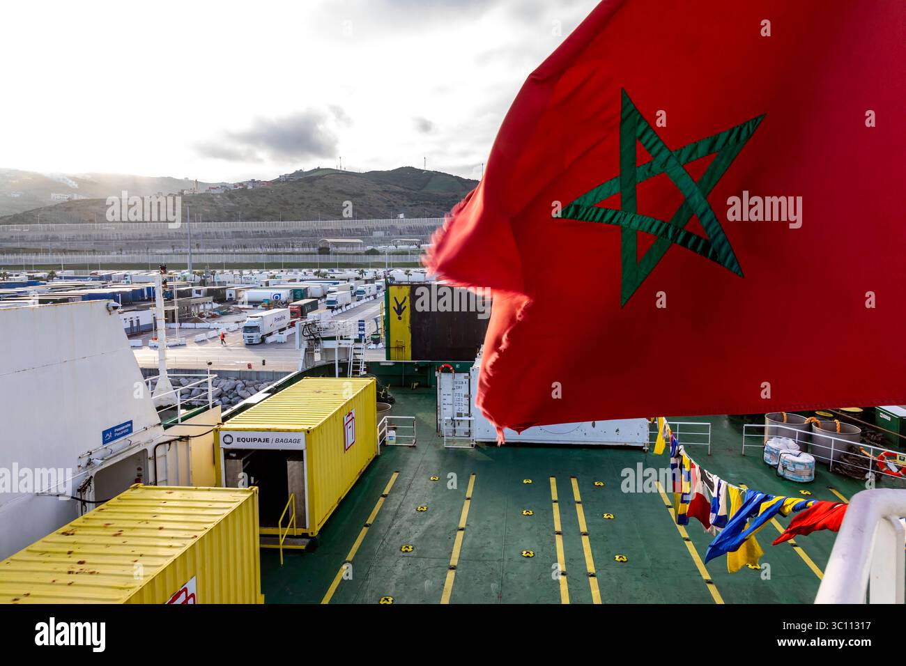 Marocco, Tangeri: Traghetto attraccato nel porto di Tangeri Med e camion in attesa di salire a bordo del traghetto. Bandiera marocchina con stella a cinque punte, bandiera rossa Foto Stock