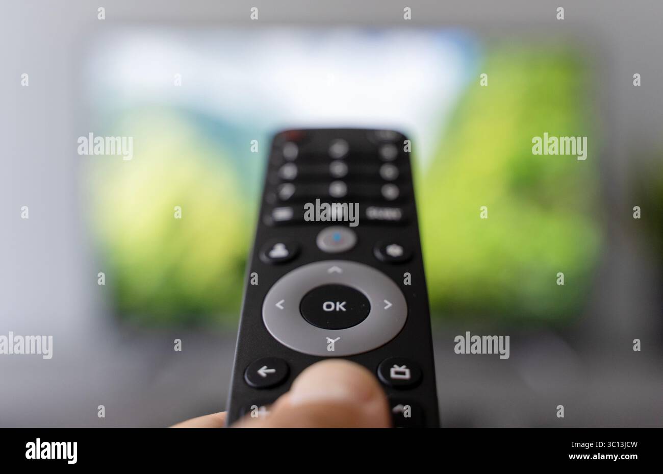 Una mano che tiene in mano il telecomando commuta i canali di un televisore con uno schermo sfocato sullo sfondo. Le riprese simboleggiano il moderno consumo dei media, il sovraccarico di contenuti, l'affaticamento delle scelte digitali e la costante ricerca di informazioni coinvolgenti. Ideale per temi riguardanti le abitudini multimediali, l'intrattenimento, l'età dell'informazione e la dipendenza dallo schermo. Foto Stock