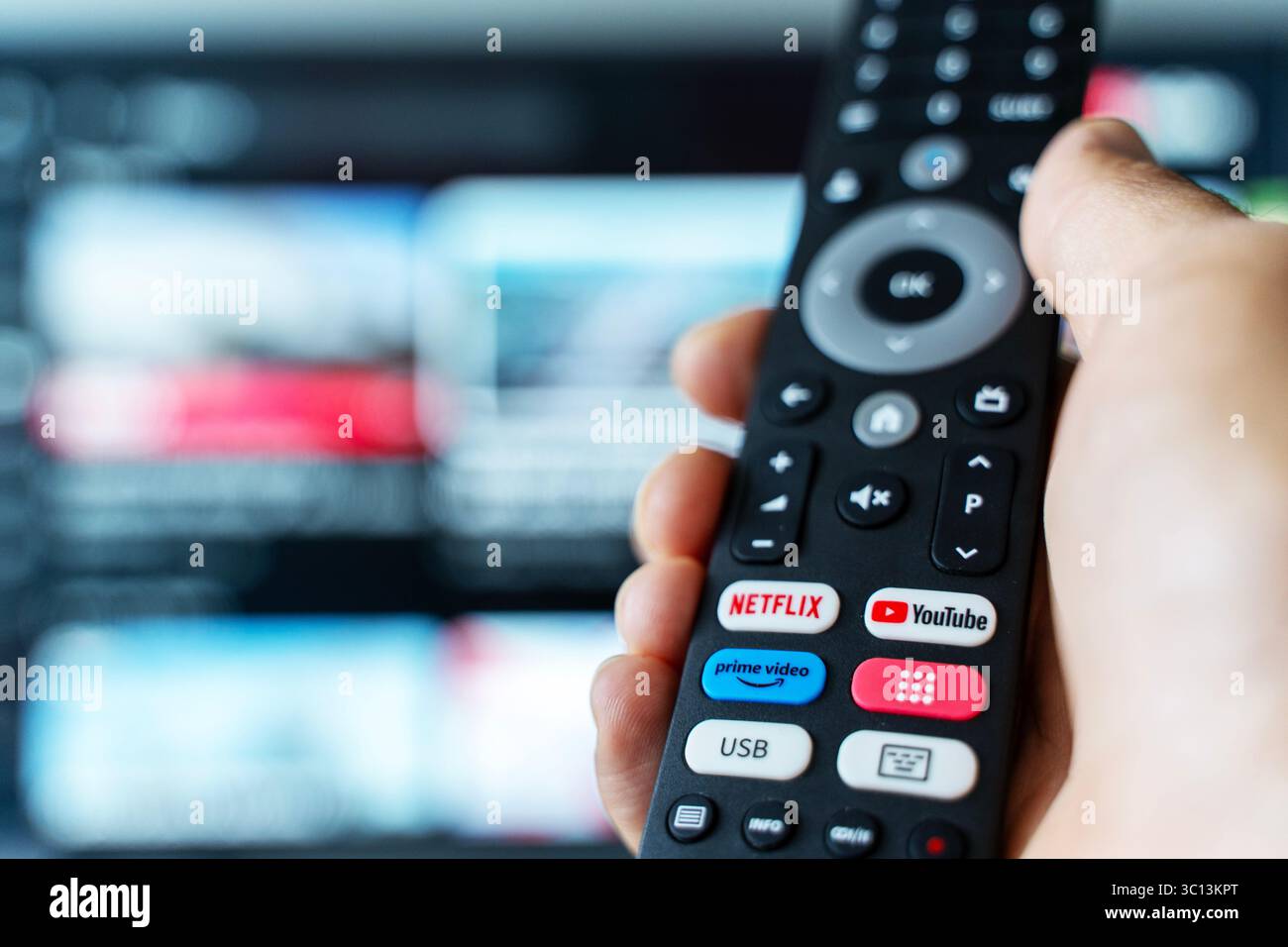 Tbilisi, Georgia - 2 luglio 2025: Foto ravvicinata di un telecomando smart TV con pulsanti dedicati per piattaforme di streaming popolari come Netflix, YouTube e Amazon prime, con uno schermo televisivo sfocato sullo sfondo. Rappresenta il consumo dei moderni media digitali, i servizi basati su abbonamento e l'intrattenimento on demand. Ideale per contenuti tecnologici, in streaming, binge-watching o media lifestyle. Foto Stock