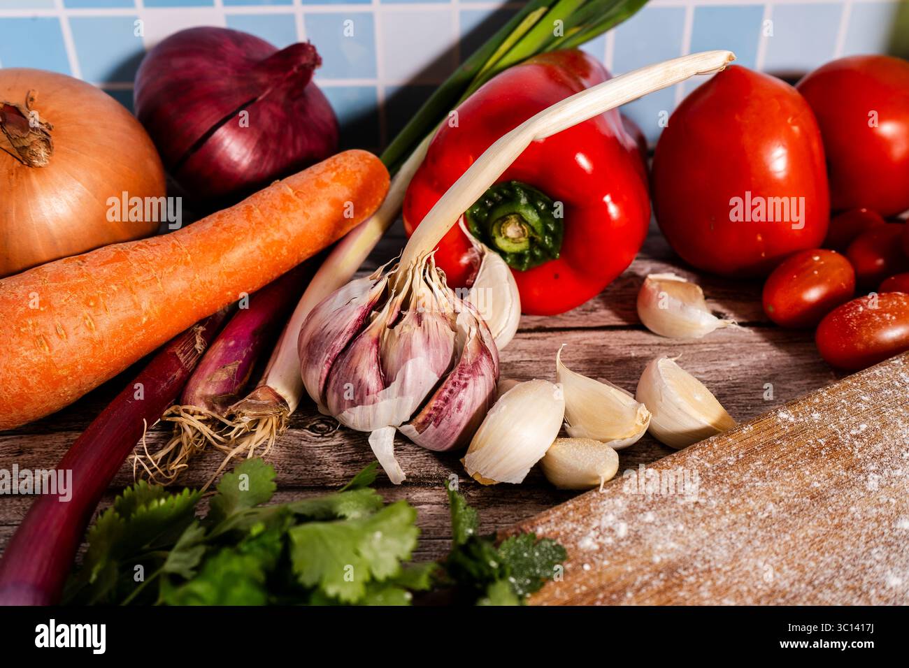 Verdure vivaci, erbe e bulbi d'aglio si appoggiano su un rustico tavolo di legno, creando un colorato spettacolo di ingredienti freschi Foto Stock