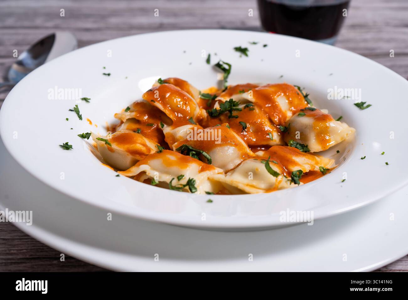 Ravioli fumanti adornati con vibrante salsa di pomodoro e prezzemolo fresco, incarnano l'essenza della tradizione culinaria italiana Foto Stock