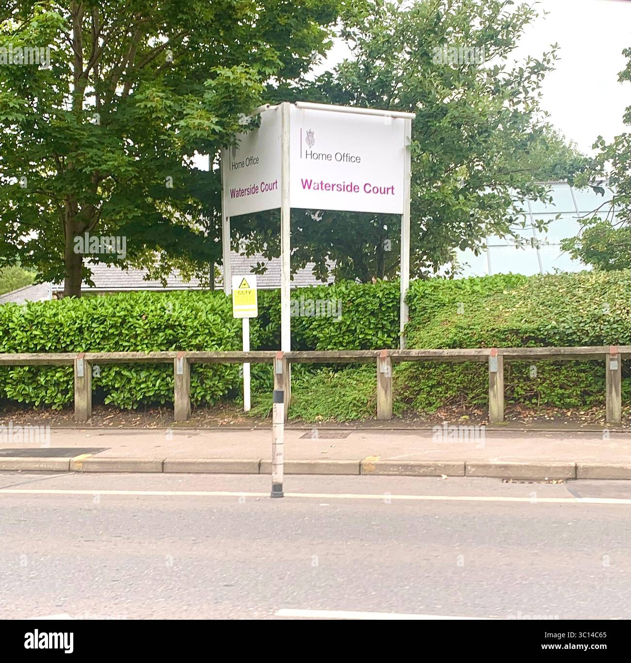 Insegna per l'Ufficio Residenziale Waterside Court situata accanto alla strada a Leeds con una grande siepe e alberi con una barriera in legno vicino alla strada principale - Immagine stock catturata con smartphone