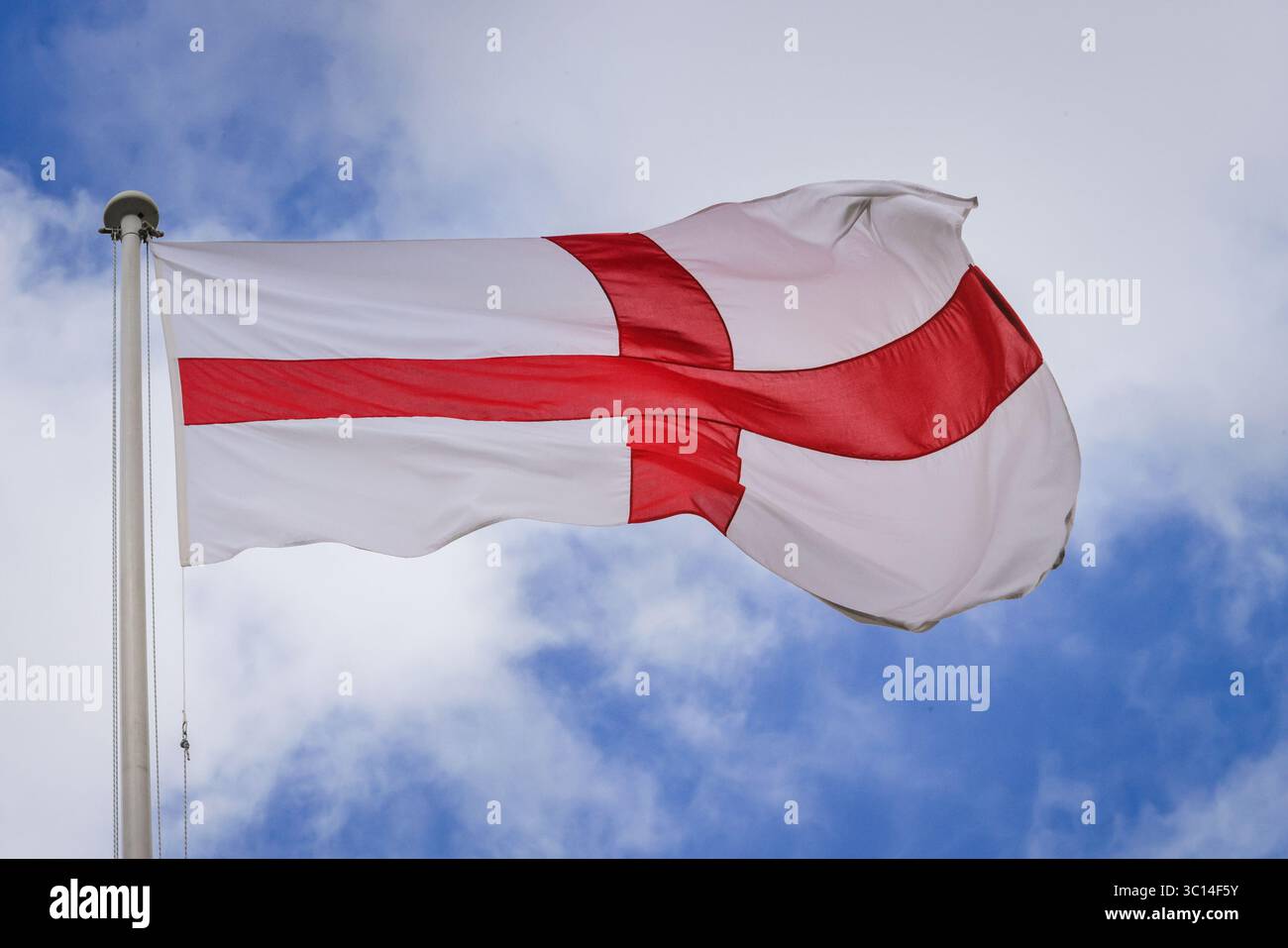Una bandiera di St George's Cross, la croce rossa su sfondo bianco della bandiera inglese, viene issata, sventolando su un palo di bandiera contro un cielo blu Foto Stock