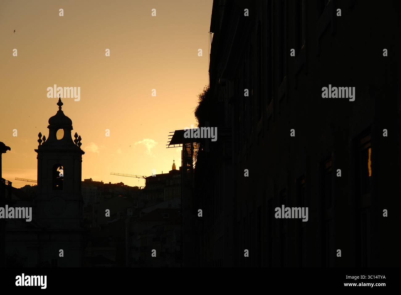Le guglie e le gru della chiesa, tutte in sillhouette, dominano il caldo tramonto di Lisbona Foto Stock Le guglie e le gru della chiesa, tutte in sillhouette, dominano il caldo tramonto di Lisbona Foto Stock