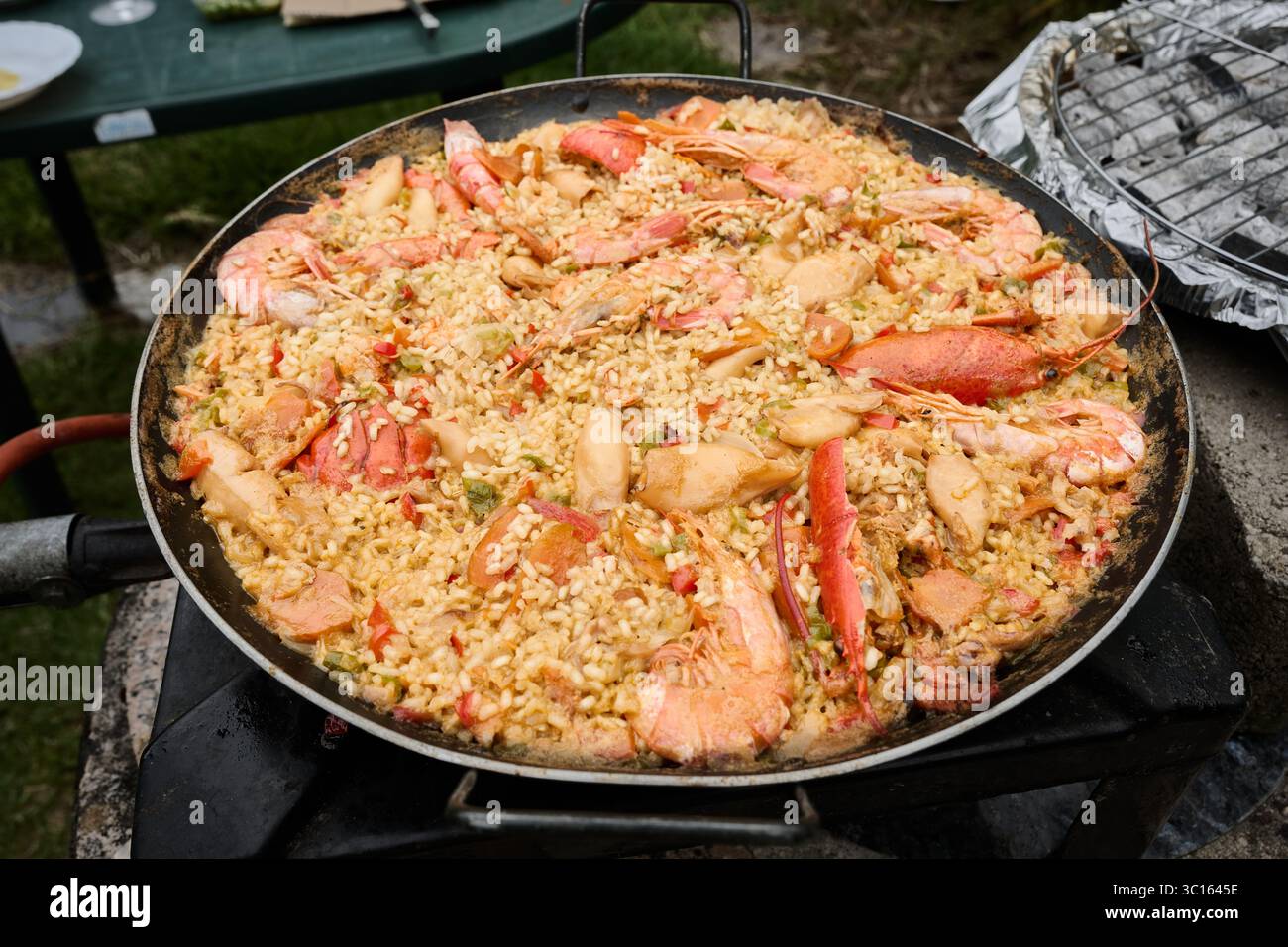 Grande padella riempita con appetitosa paella di pesce che sogna su una stufa da campeggio, che mostra colori vivaci e ricchi sapori all'aperto Foto Stock