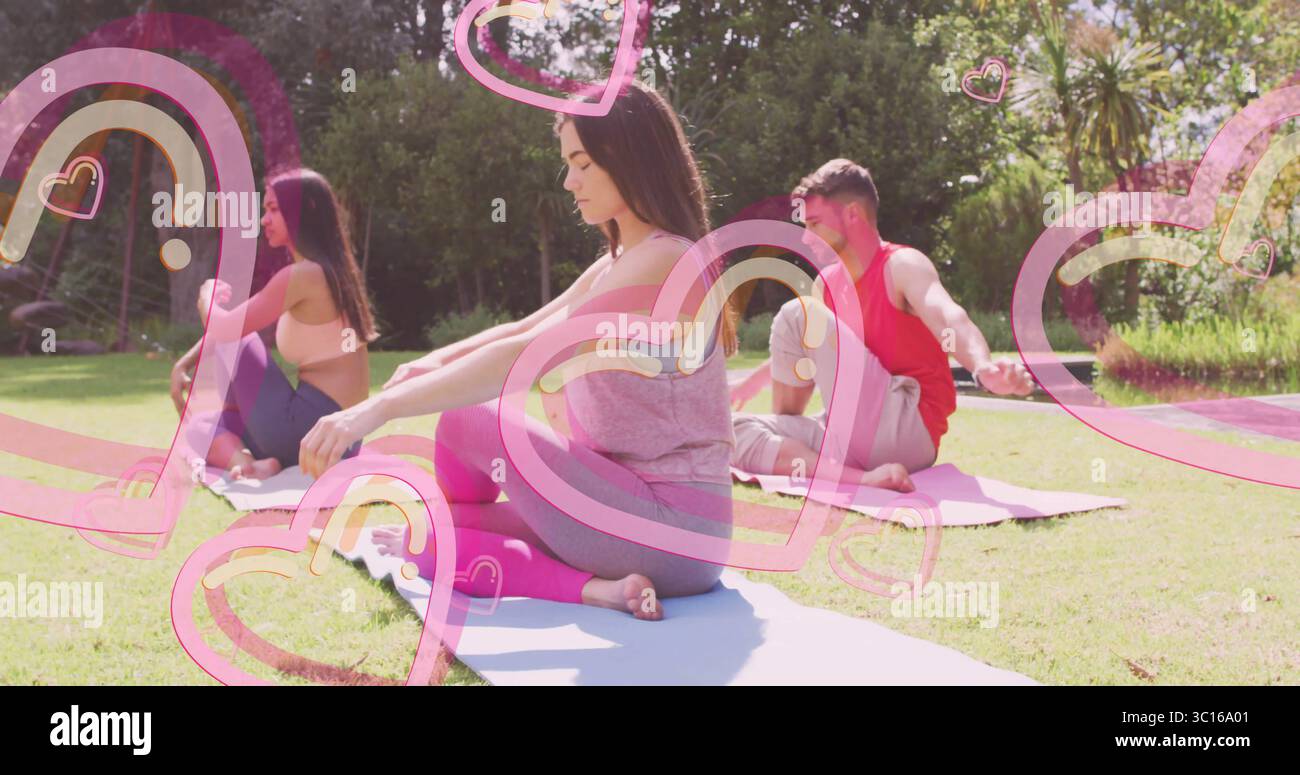 Esercitarsi con tre amici seduti a gambe incrociate su tappetini da yoga nel giardino sul retro, con grafica a cuore Foto Stock