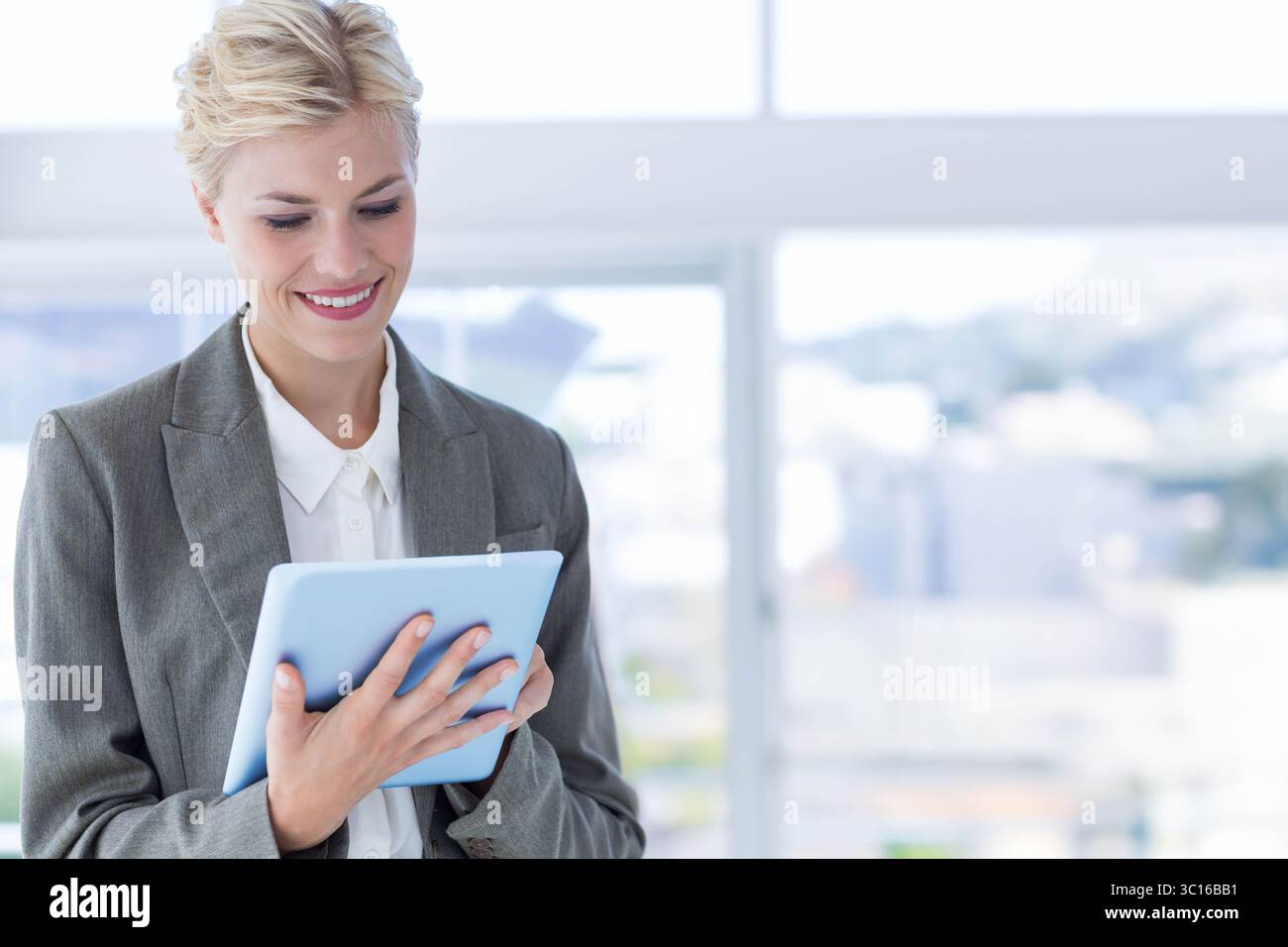Dispositivo tablet posizionato in un luminoso interno dell'ufficio, accanto a un'ampia finestra che mostra lo skyline urbano sfocato Foto Stock