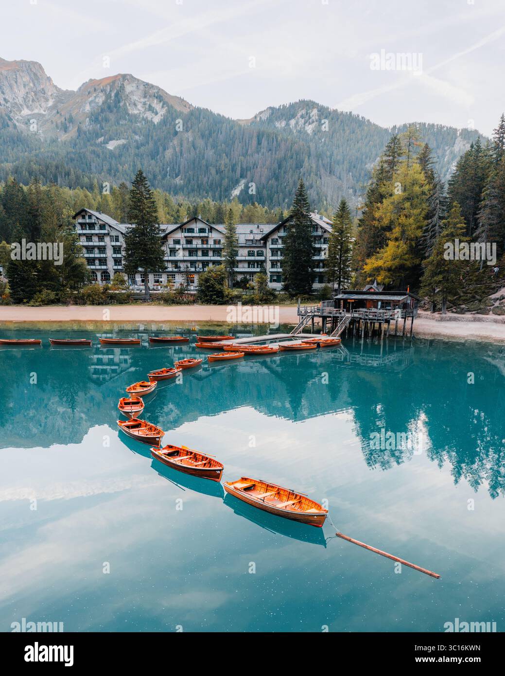 Veduta aerea di una linea di barche a remi ormeggiate sulle acque turchesi del Lago di Braies, sullo sfondo di montagne e alberi sempreverdi, Prags, Trentino-alto Adige, Italia. Foto Stock
