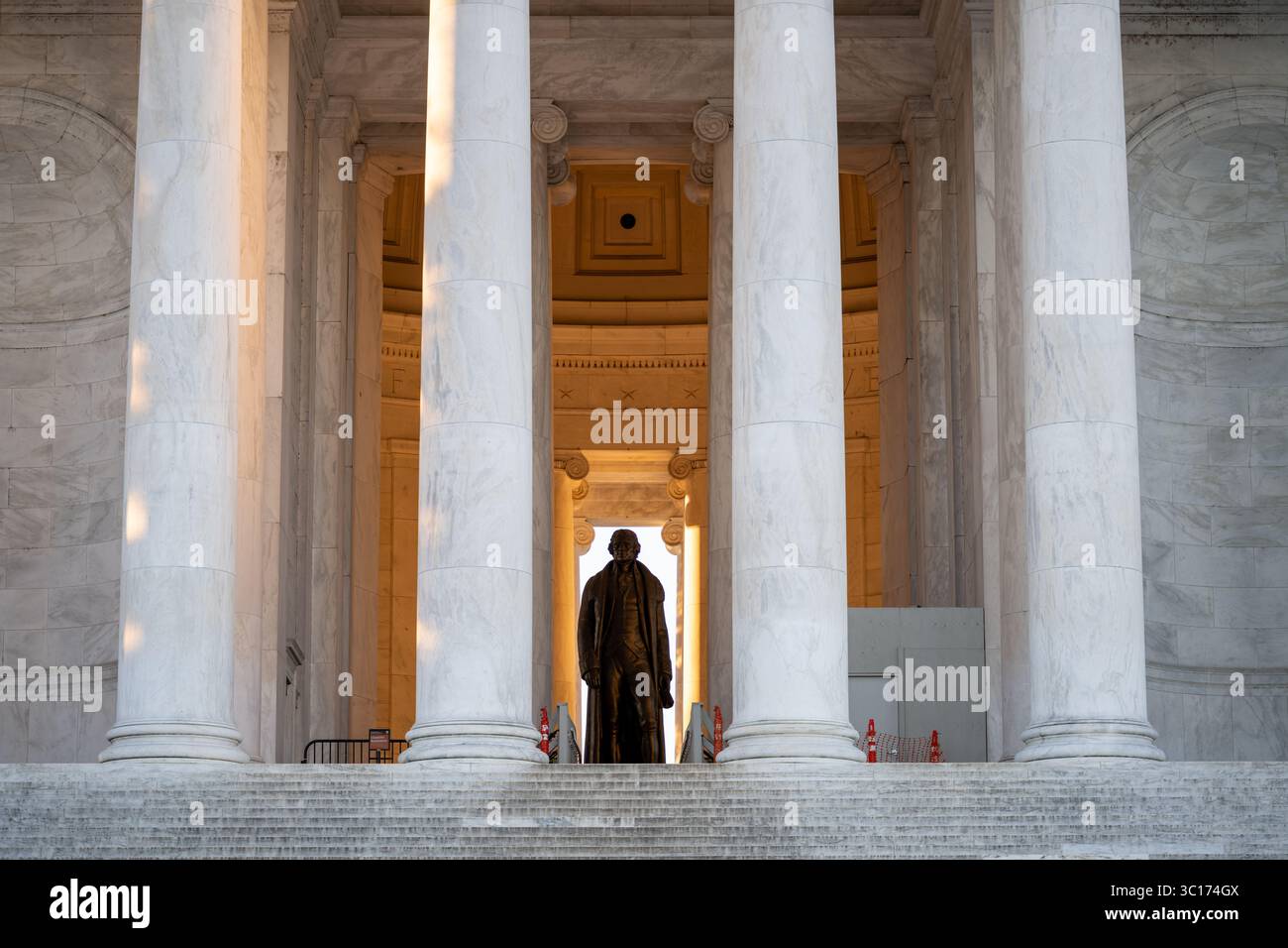 Jefferson Memorial Statue Washington DC // WASHINGTON DC — la statua di bronzo di Thomas Jefferson è visibile attraverso le colonne del portico nord del Jefferson Memorial, con luce solare dorata che illumina la camera principale subito dopo l'alba. La statua di 5,8 metri, creata dallo scultore Rudulph Evans, raffigura il terzo presidente degli Stati Uniti e autore principale della dichiarazione di indipendenza. Il Jefferson Memorial, completato nel 1943, fu progettato dall'architetto John Russell Pope in stile neoclassico con un colonnato circolare di colonne ioniche. Il memoriale si trova sul bacino delle maree e. Foto Stock