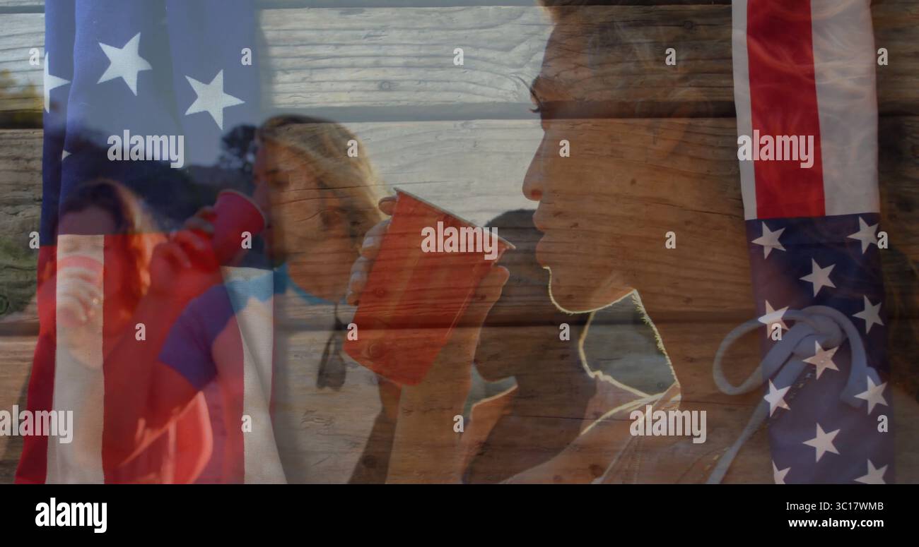 Bevendo amici che tengono in mano tazze di plastica rosse sulla riva del lago durante il tramonto, copertura bandiera americana Foto Stock