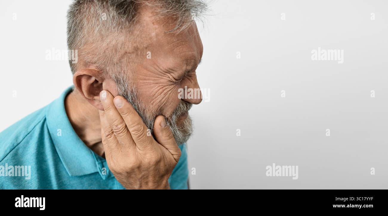 Un uomo anziano tocca l'orecchio, mostrando disagio per problemi uditivi in un ambiente chiuso e calmo Foto Stock