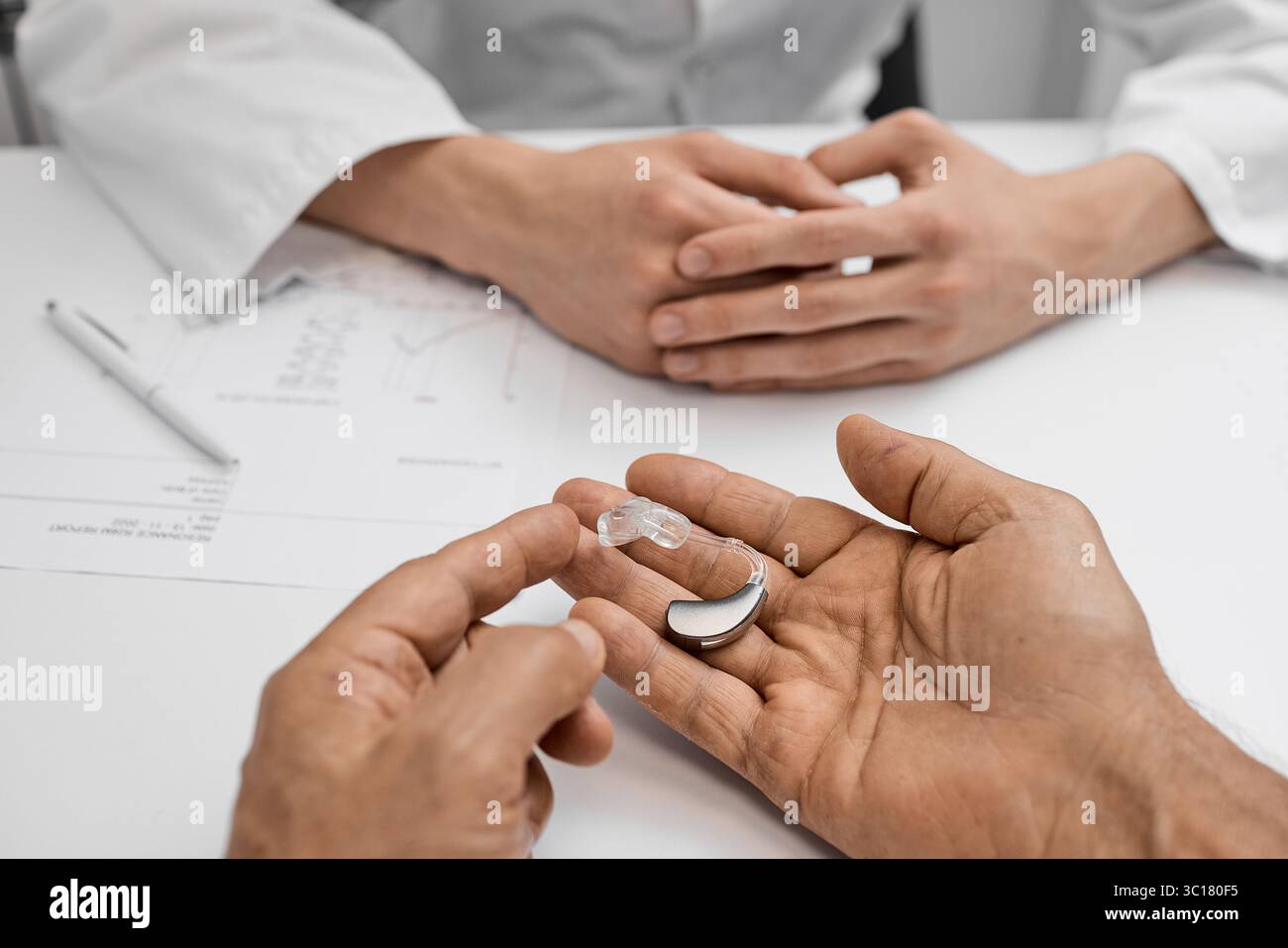 Concetto di audiologia. Il medico/audiologo discute le opzioni degli apparecchi acustici con il paziente, mostrando le caratteristiche del dispositivo durante la consultazione uditiva Foto Stock