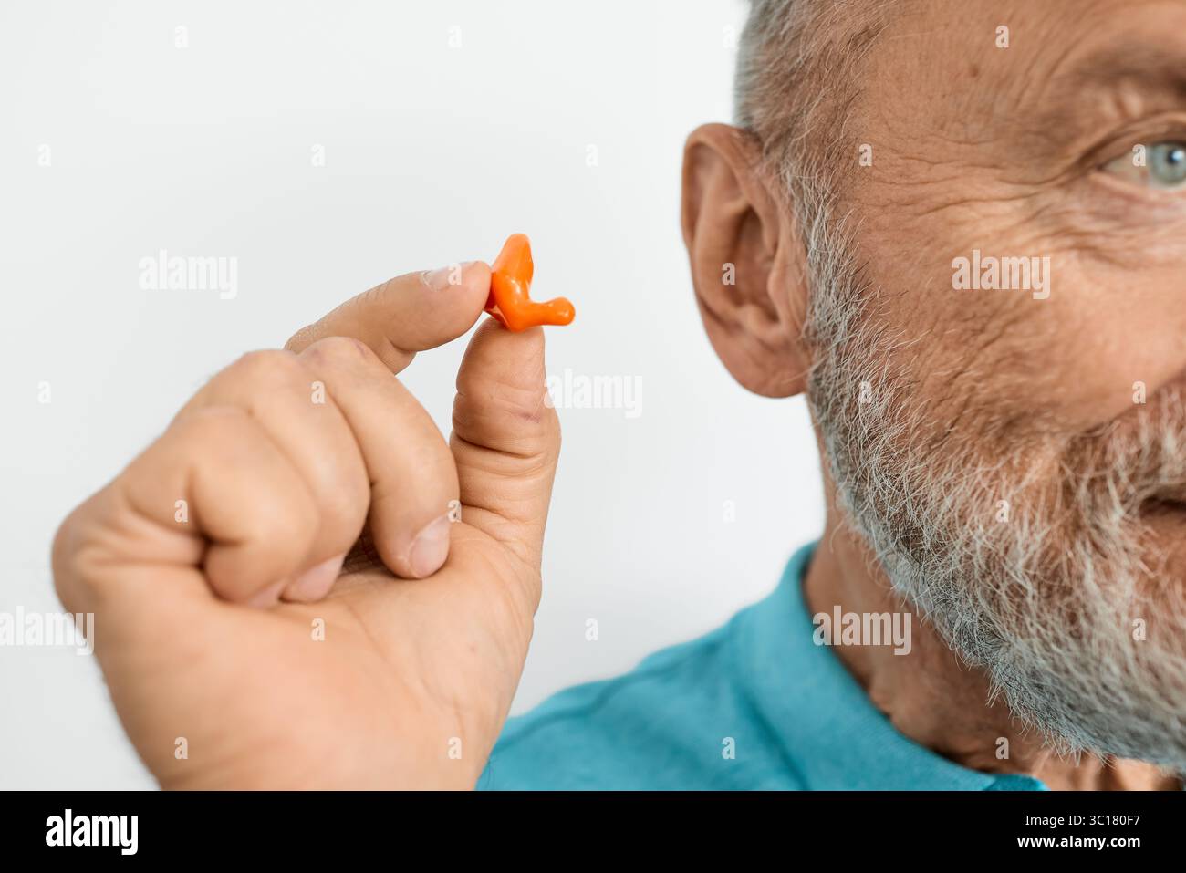 Isolato su un tappo auricolare bianco vicino all'orecchio dell'uomo anziano. tappi auricolari stampati personalmente, primo piano Foto Stock