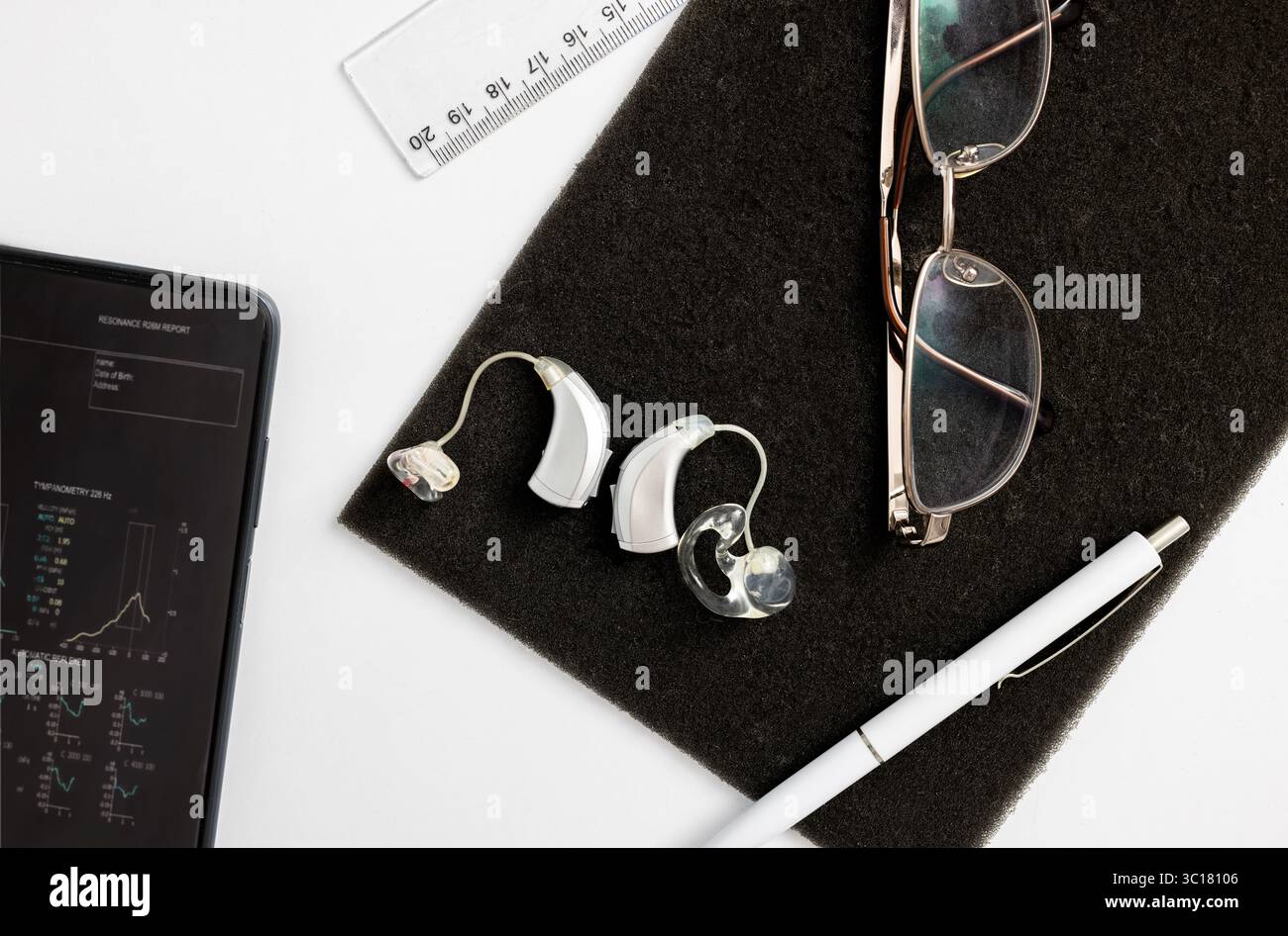 Vista aerea di apparecchi acustici, occhiali e tablet su una superficie scura, che mette in risalto gli accessori essenziali degli utenti aziendali che indossano apparecchi acustici Foto Stock