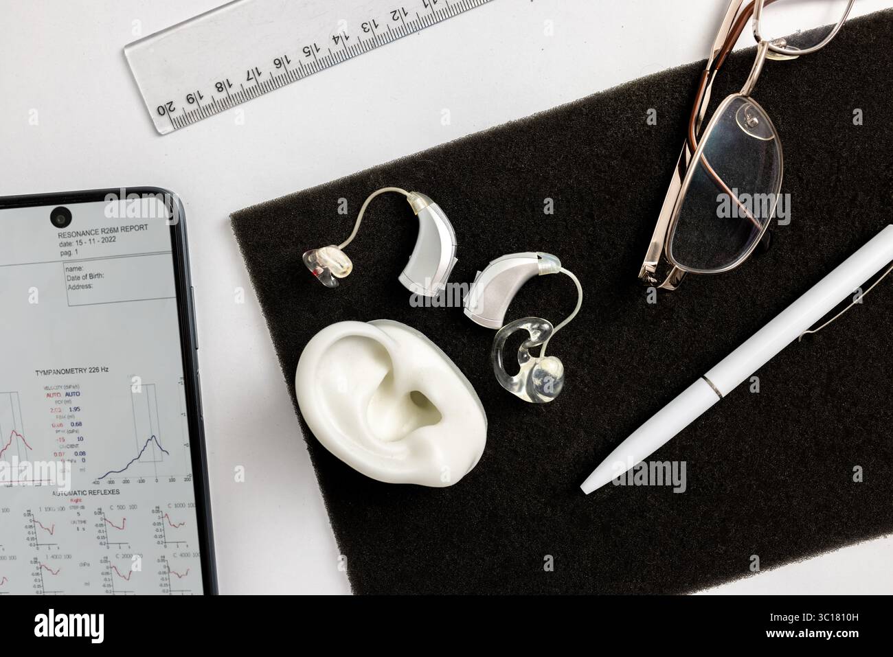 Concetto di audiologia. Gli apparecchi acustici avanzati sono dotati di una superficie minimalista con vetri e un blocco note, mettendo in risalto la tecnologia moderna e lo stile aziendale Foto Stock