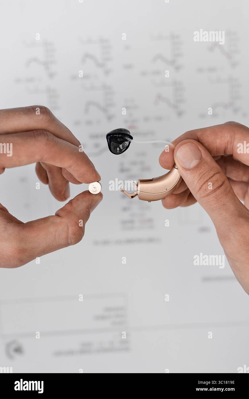 Audiologo che mostra a un paziente di una clinica uditiva come sostituire le batterie per l'apparecchio acustico per la manutenzione. Soluzioni per l'udito Foto Stock