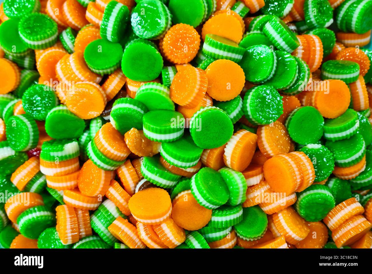 Un accattivante assortimento di caramelle rotonde in gelatina dalle vivaci tonalità verde e arancione con strisce bianche a strati. Una collezione di dolcetti colorati e dolci Foto Stock