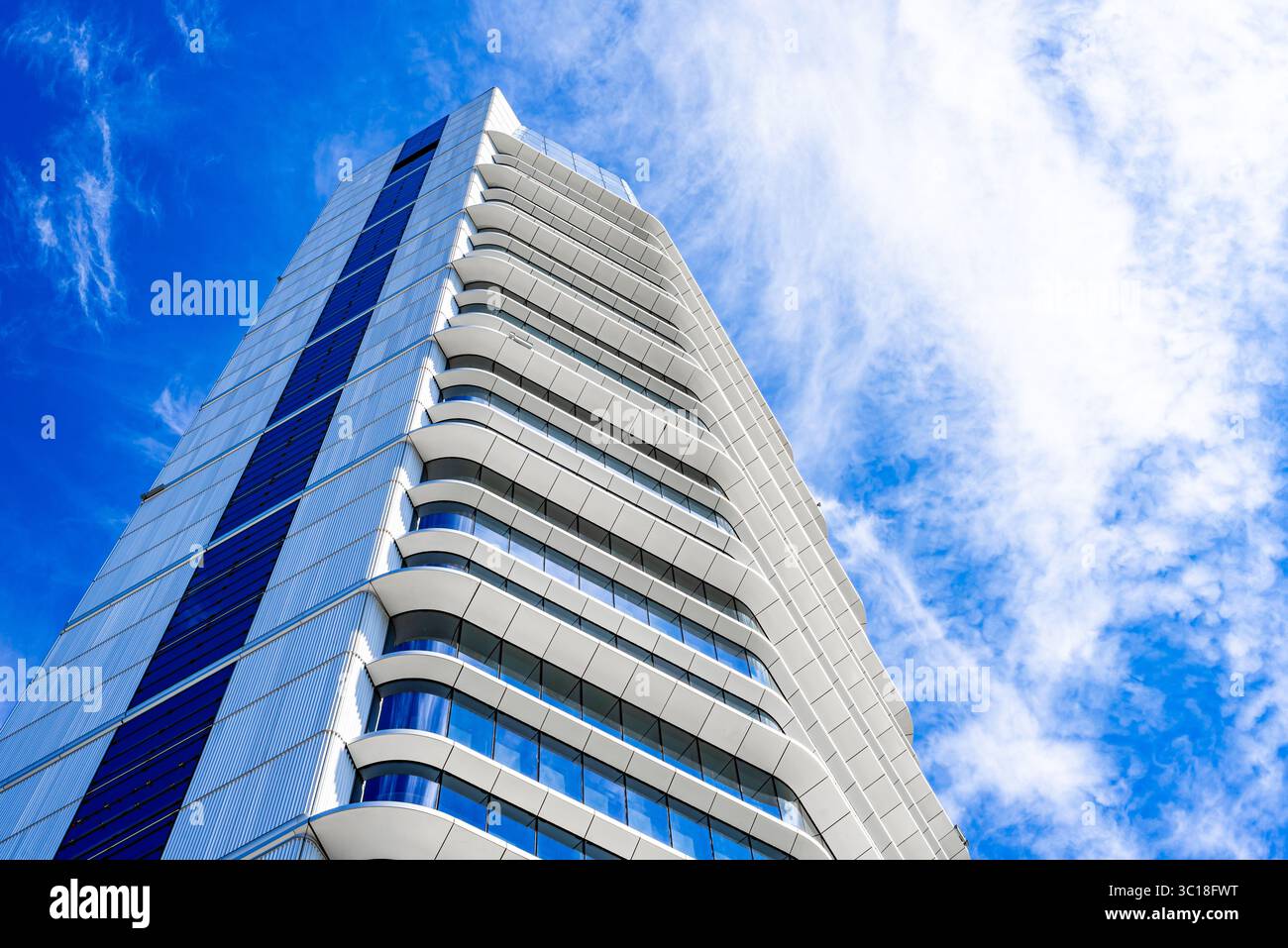 Moderno edificio residenziale a più piani con facciata vivace, grandi balconi e skyline urbano sotto il cielo azzurro Foto Stock