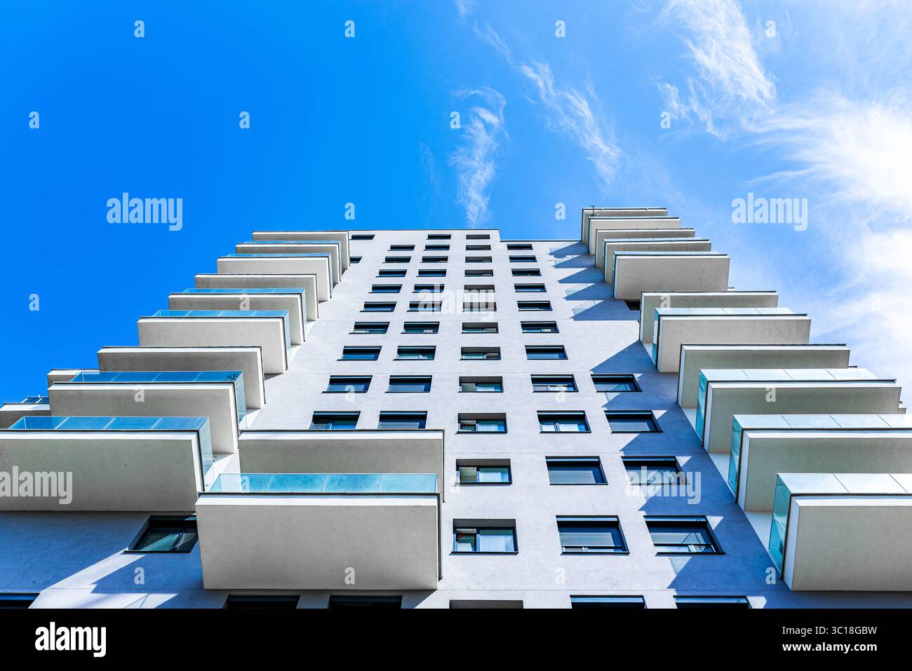 Moderno edificio residenziale a più piani con facciata vivace, grandi balconi e skyline urbano sotto il cielo azzurro Foto Stock