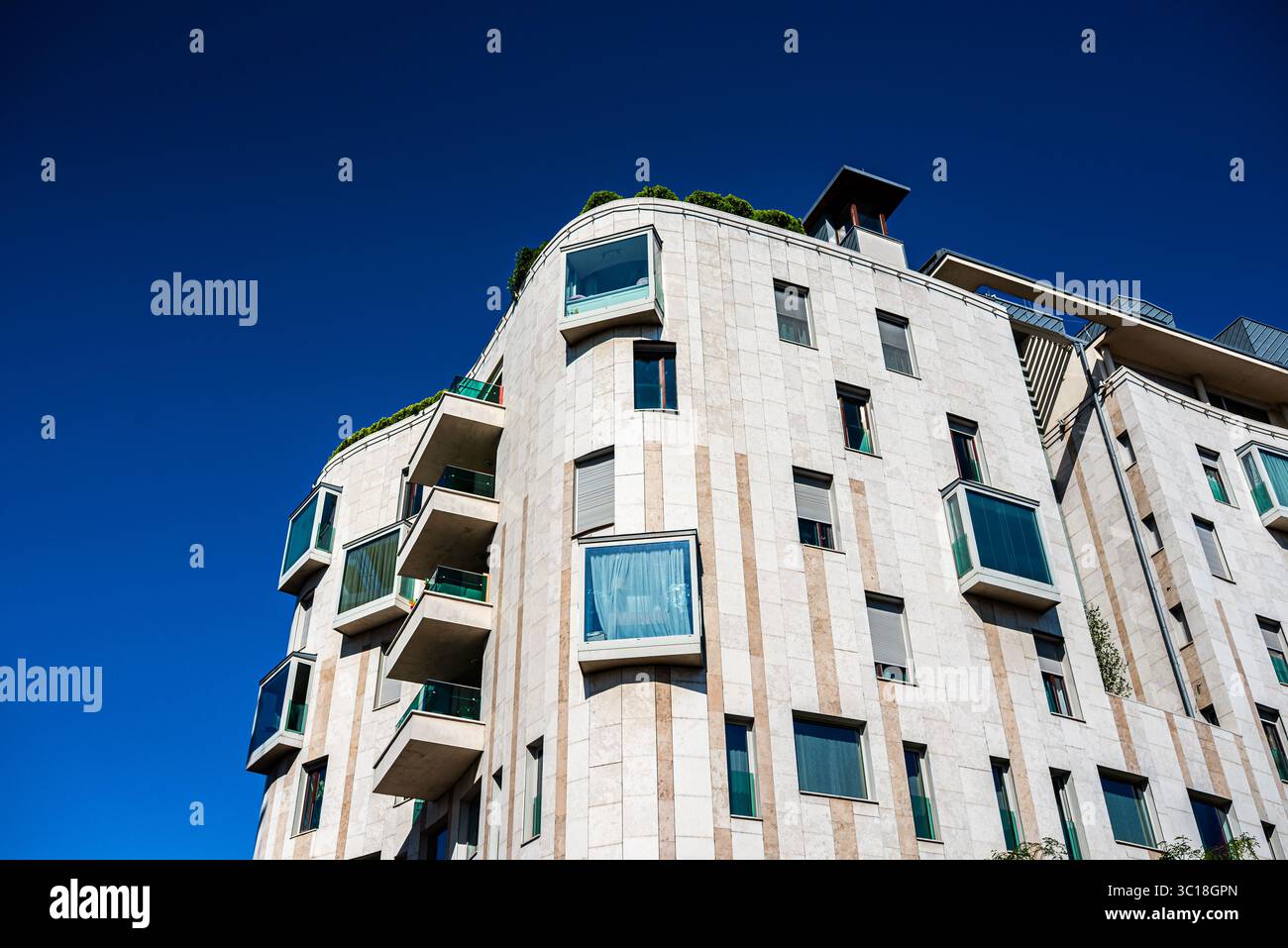 Edifici residenziali contemporanei con balconi moderni, facciate in mattoni e riflessi sotto un cielo limpido Foto Stock