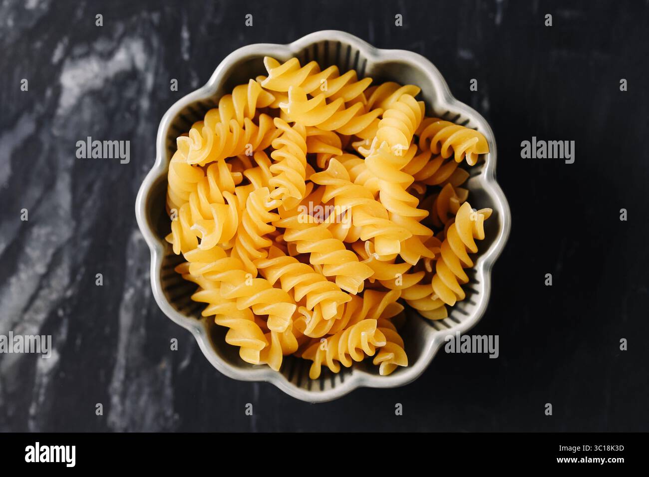 Penne crude nel recipiente. Spaghetti secchi gialli su sfondo scuro. Primo piano sui maccheroni italiani crudi. Ingredienti alimentari tradizionali. Pasto semplice e salutare. Foto Stock