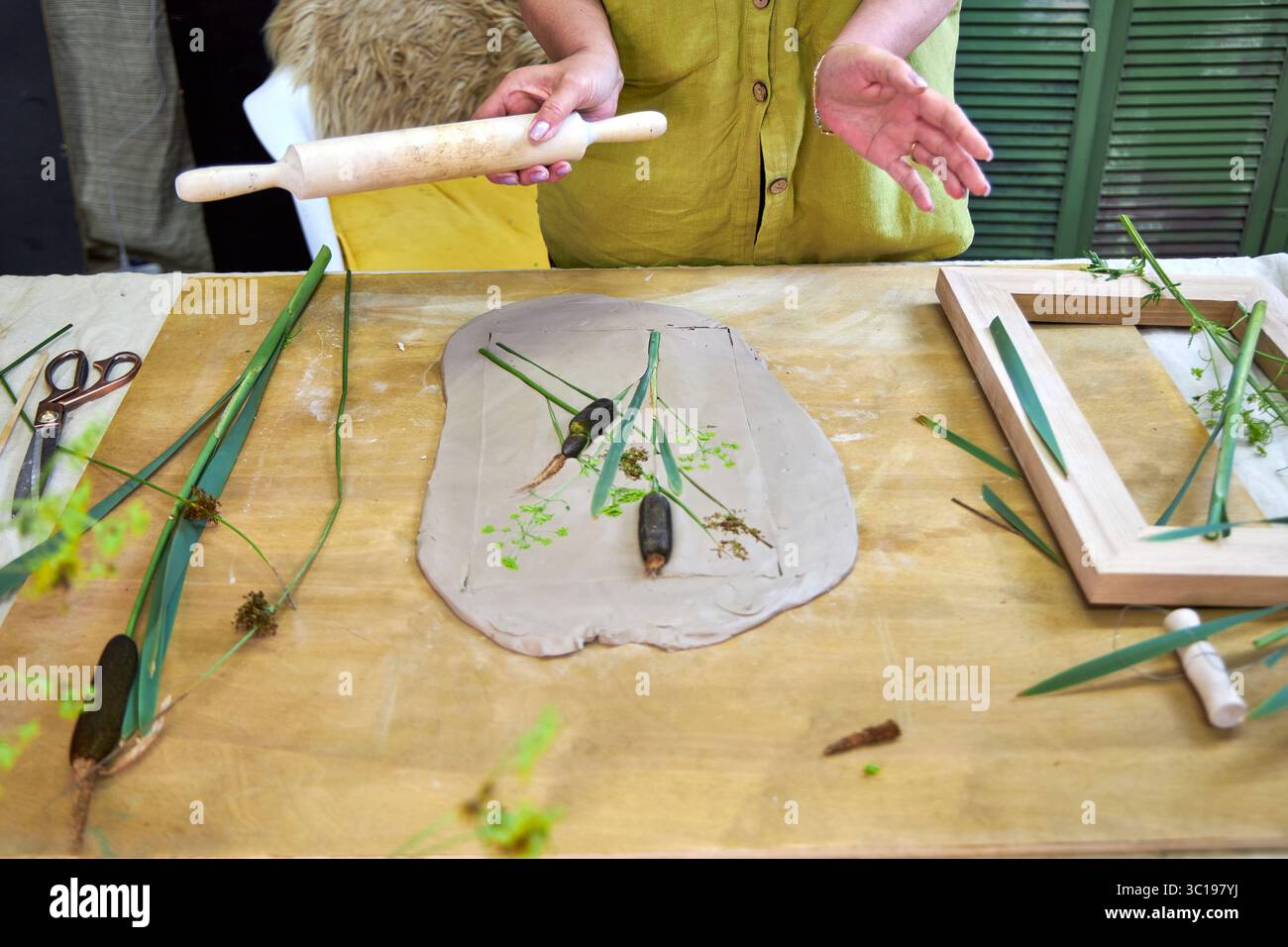 Premendo fiori e foglie in argilla con un mattarello per creare un'impronta botanica per il rilievo gesso. Mani appiattimento piante in fai da te passo per passo t Foto Stock