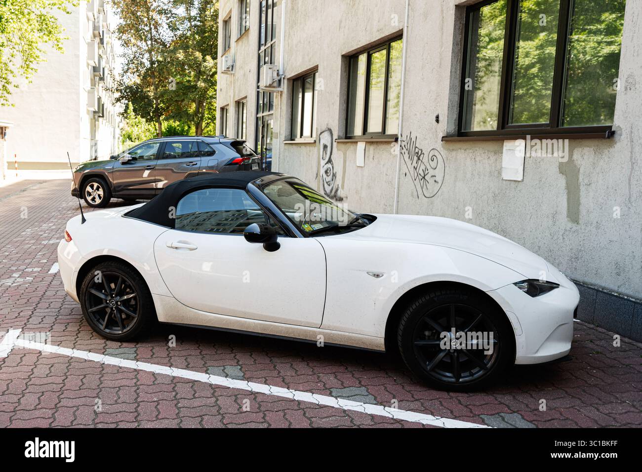 Varsavia, Polonia - 2 luglio 2025: Una moderna Mazda MX-5 bianca convertibile sotto la luce del sole a Varsavia accanto a un edificio urbano. Foto Stock