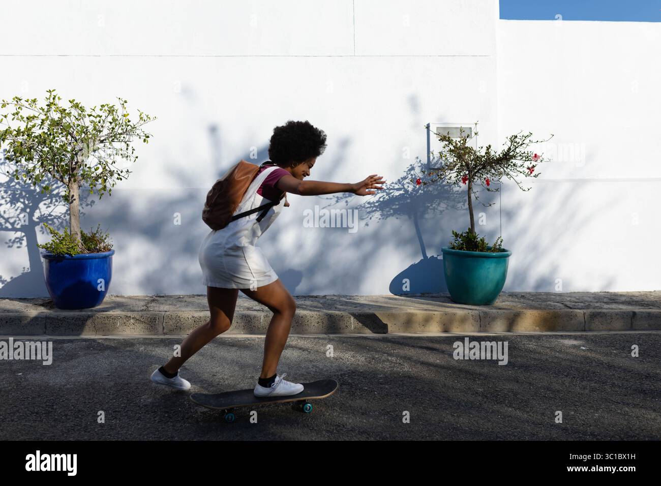 Skateboarder inclinato in avanti e in equilibrio sulla strada vicino a pareti bianche con vasi colorati per piantatrici Foto Stock