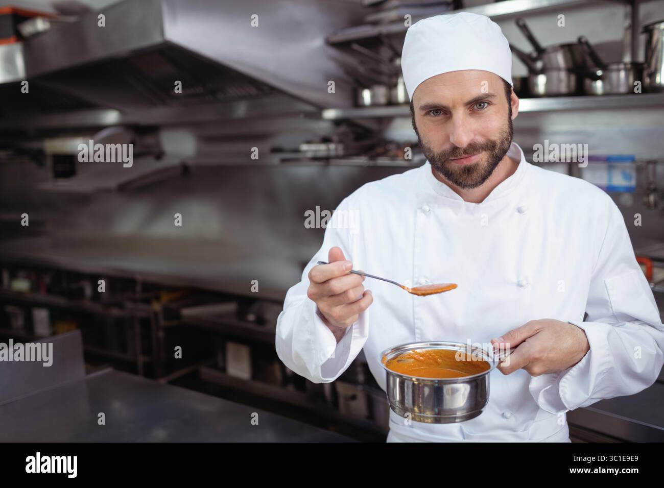 Chef maschile professionista che tiene in mano una pentola e degusta zuppa di pomodoro in cucina commerciale, spazio per copiare Foto Stock