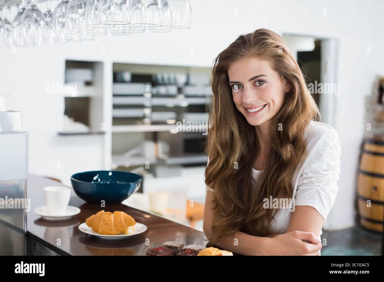 Donna appoggiata su un bancone di legno in un luminoso caffè con piatto di croissant e tazza di caffè, spazio per fotocopie Foto Stock
