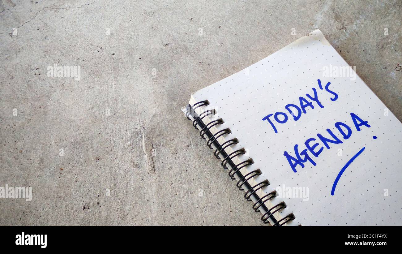 L'agenda di oggi è scritta a mano in un notebook Dot-Grid su uno sfondo di cemento incrinato Foto Stock