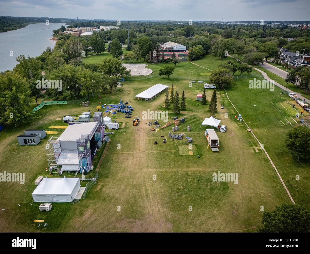 Grande campo con tende e palcoscenico allestito per un festival. L'erba è verde e il cielo è nuvoloso Foto Stock