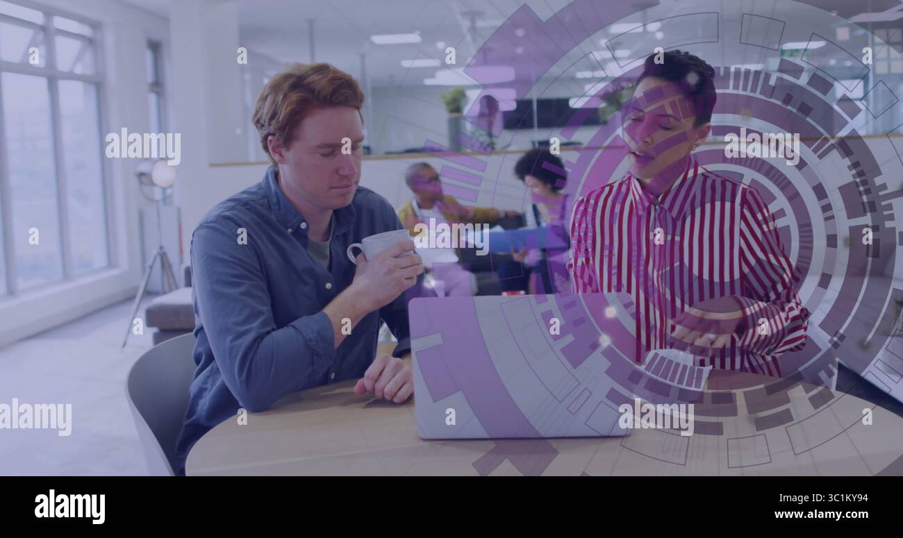 Due colleghi che indossano camicie da lavoro discutono del progetto al tavolo in ufficio, con laptop e tazza Foto Stock
