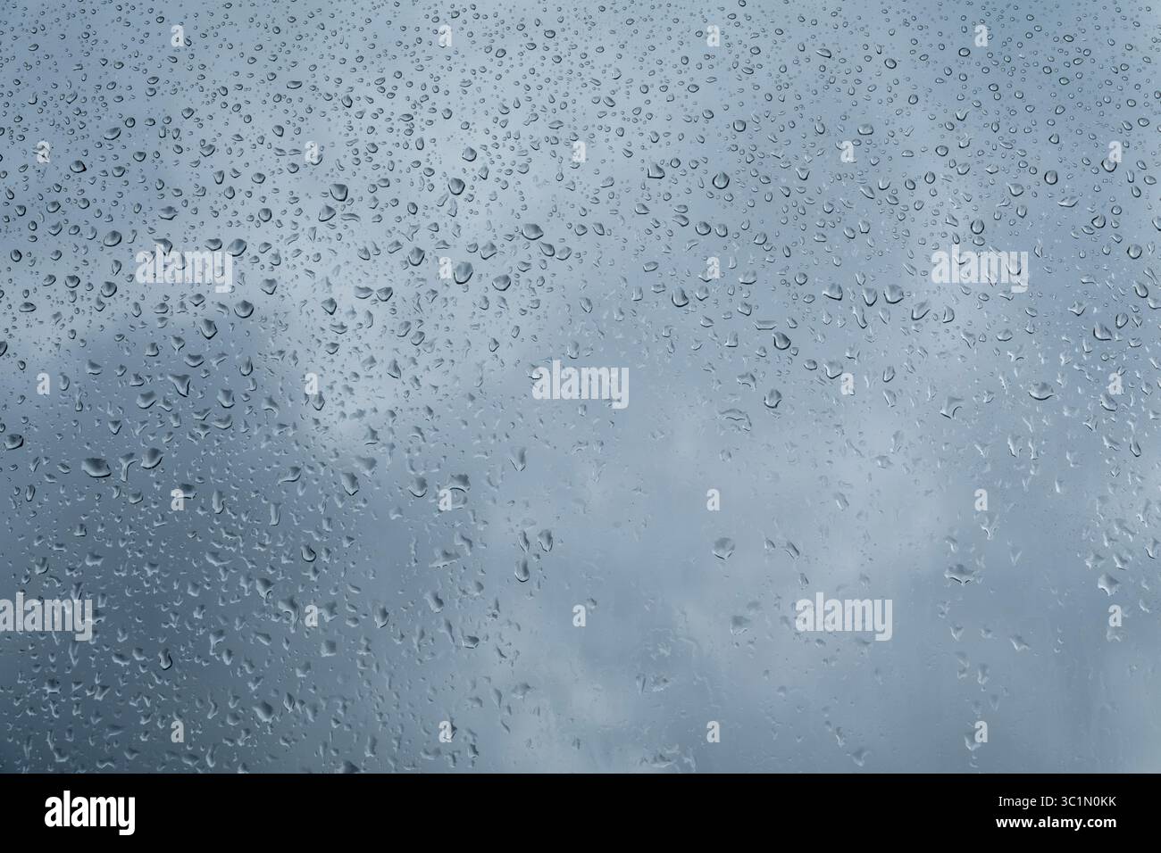 L'acqua cade sul pannello. Gocce d'acqua sul vetro della finestra. Cielo nuvoloso blu sullo sfondo. Vapore acqueo condensato sul pannello della finestra. Foto Stock
