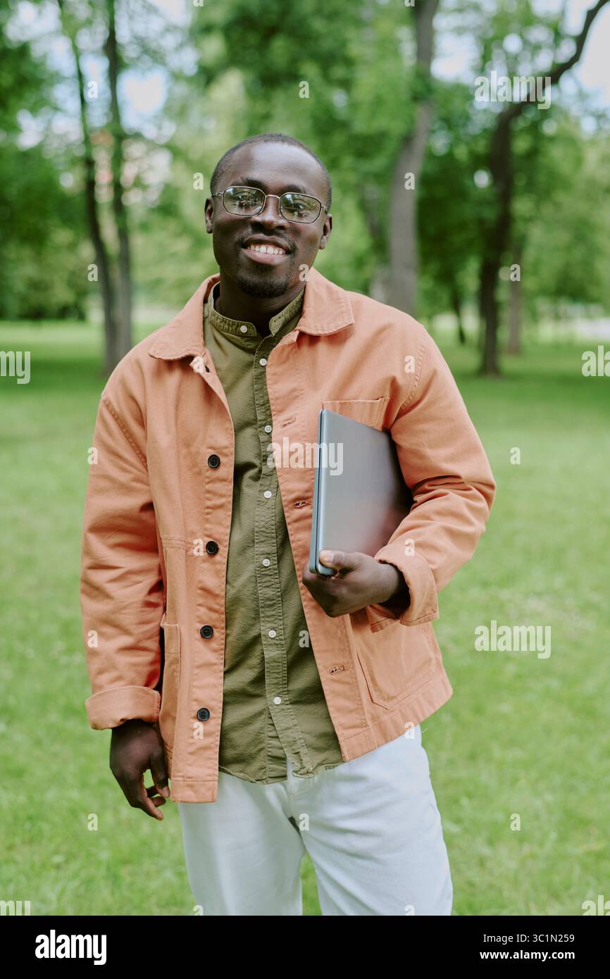 Ritratto di un giovane uomo nero che sorride e tiene in mano un laptop a Park Foto Stock