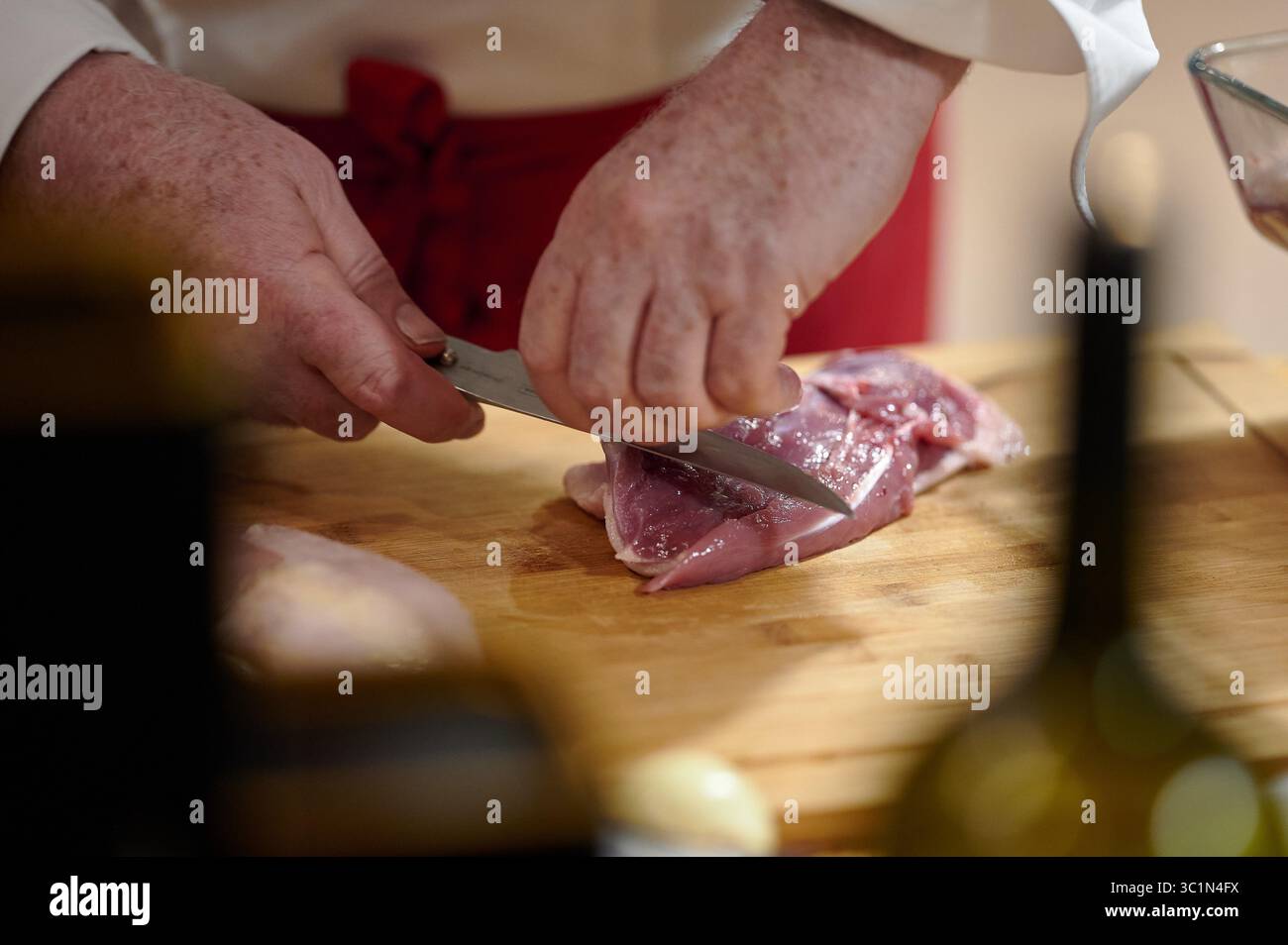 Lo chef affetta sapientemente carne cruda su tagliere di legno Foto Stock