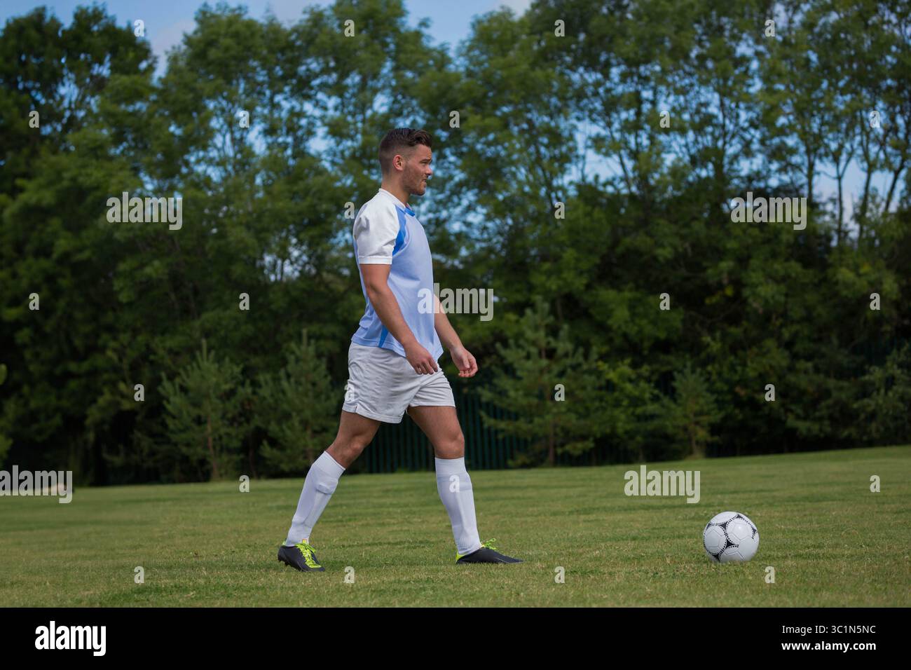 Giocatore di calcio maschile che cammina su un campo in erba e dribbling di palle da calcio con maglia blu e scarpe da calcio Foto Stock Giocatore di calcio maschile che cammina su un campo in erba e dribbling di palle da calcio con maglia blu e scarpe da calcio Foto Stock