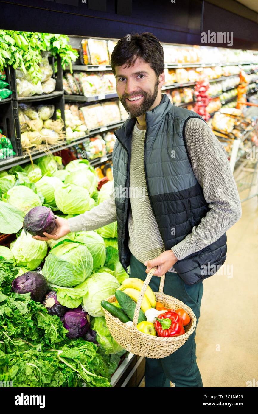 Uomo di mezza età che raccoglie il cavolo viola e tiene un cesto con banane nel corridoio dei prodotti del supermercato Foto Stock
