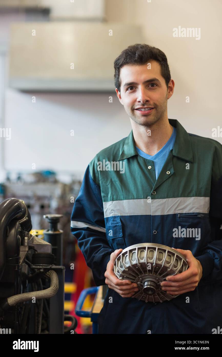 Uomo in tuta che tiene il componente accanto al cavalletto del motore in officina vicino al cofano superiore, spazio di copia Foto Stock