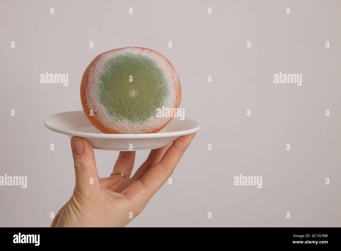 Arancione ammuffito con fungo verde su un piatto, che illustra il deterioramento degli alimenti, la contaminazione e i rischi per la salute Foto Stock