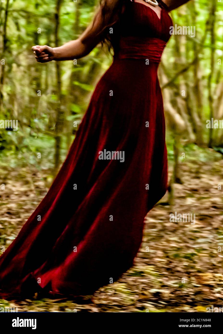 Una donna con un vestito rosso che scorre corre attraverso una foresta. Foto Stock