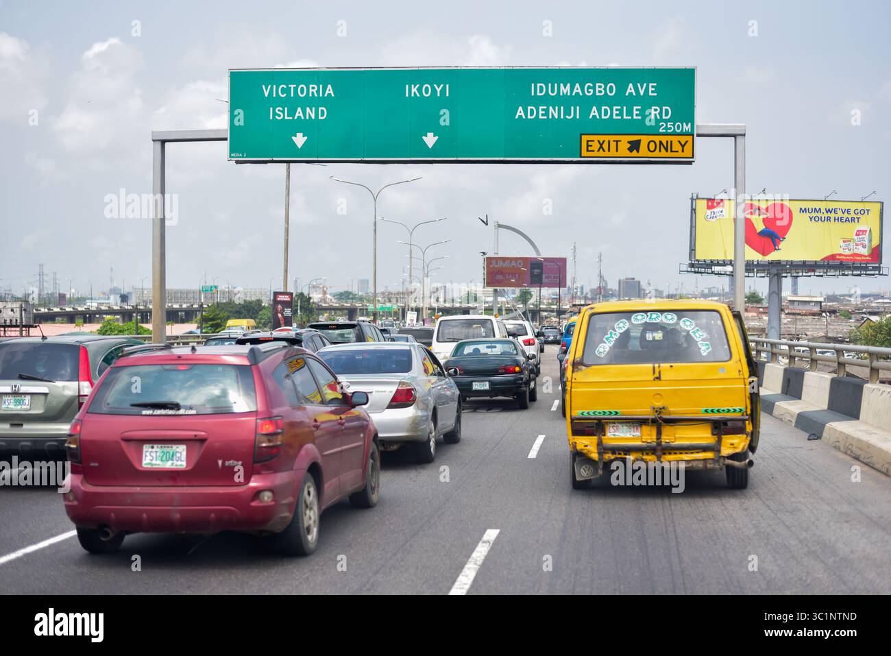 Lagos, Nigeria - 14 giugno 2022: Autobus commerciale giallo Lagos "Danfo" che guida lungo il ponte di Obalende con cartelli stradali sullo sfondo Foto Stock