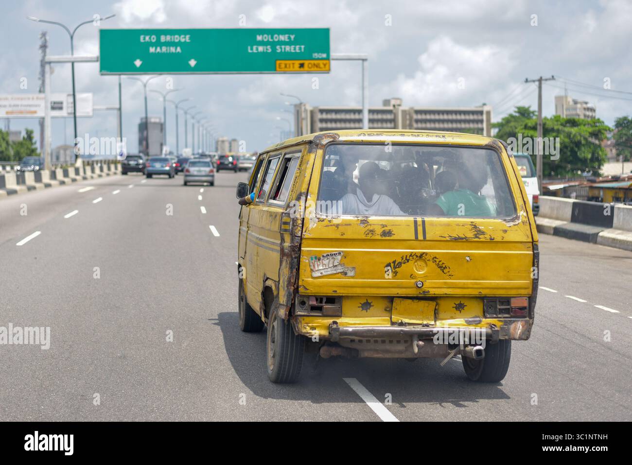Lagos, Nigeria - 14 giugno 2022: Autobus commerciale giallo Lagos "Danfo" che guida lungo il ponte di Obalende con cartelli stradali sullo sfondo Foto Stock