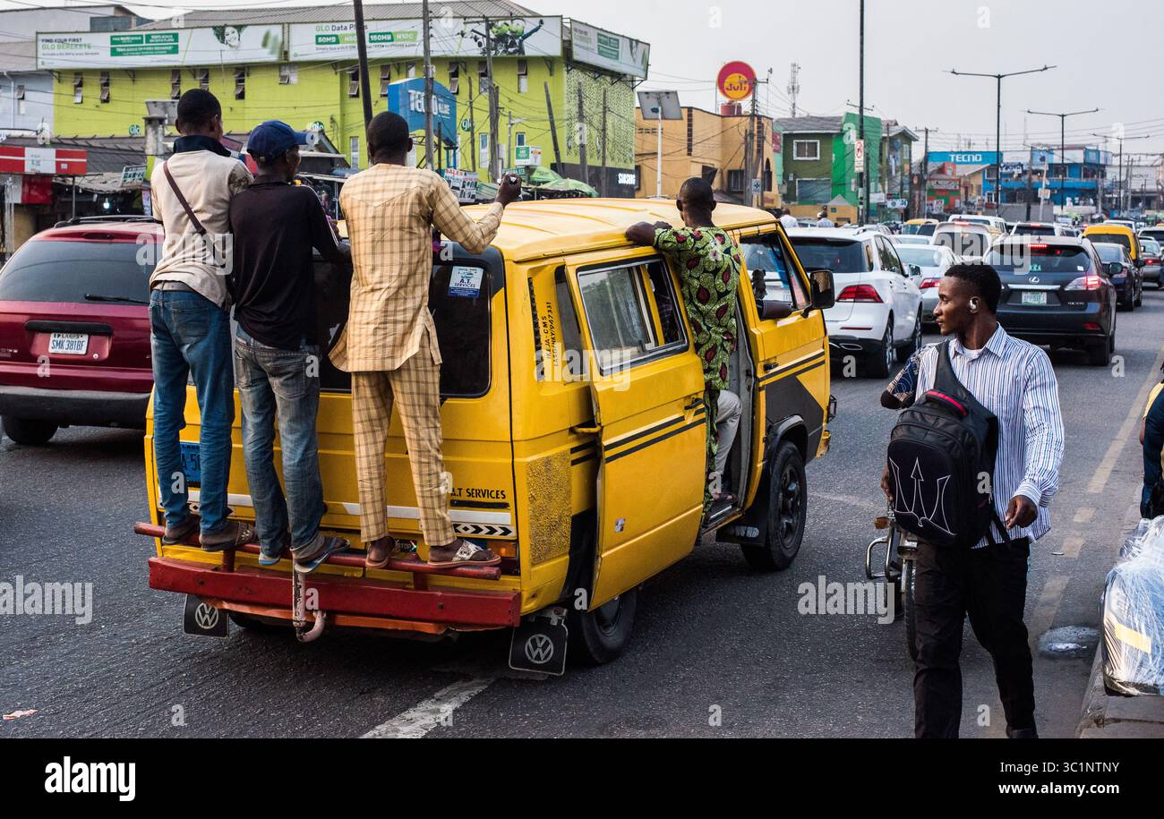 Lagos, Nigeria – 18 gennaio 2022: I passeggeri si aggrappano alle spalle di un autobus danfo giallo in movimento nel traffico intenso, illustrando le lotte quotidiane e un Foto Stock