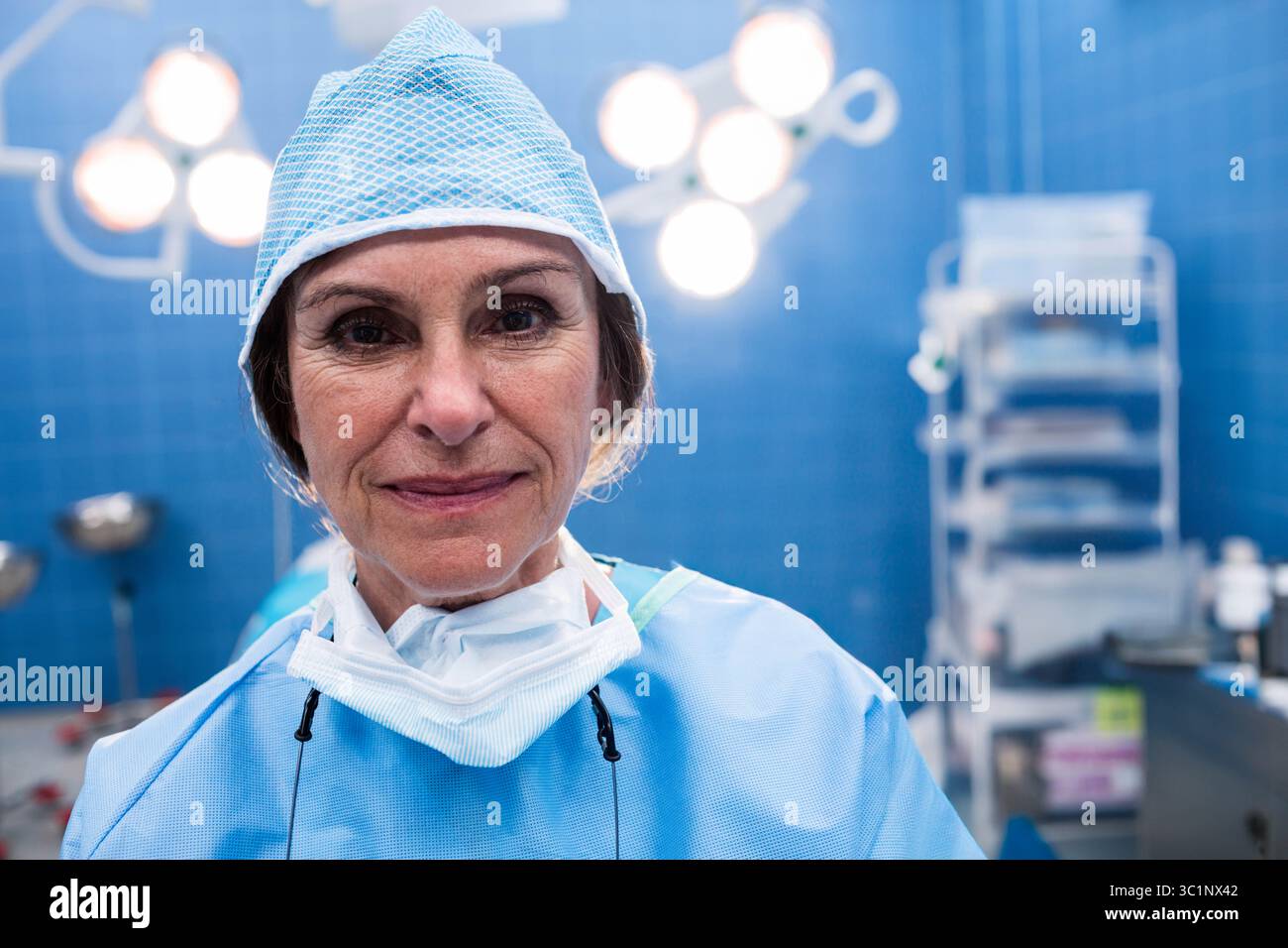 Il chirurgo senior si trova sotto le luci chirurgiche luminose nella sala operatoria con ciotole e carrello Foto Stock