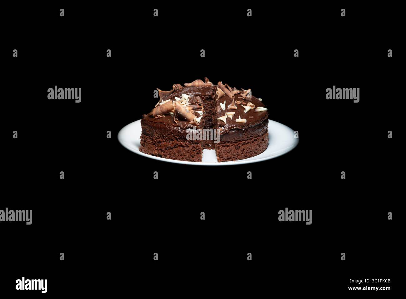 Torta al cioccolato con una fetta rimossa, ricoperta di scaglie di cioccolato e servita su un piatto bianco su sfondo nero. Foto Stock