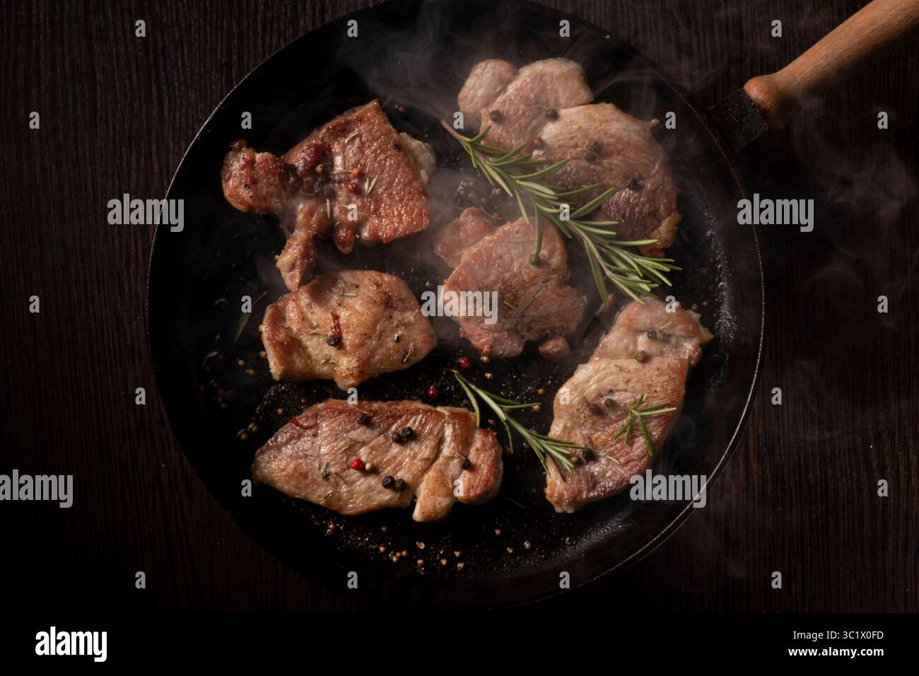 Uno shot ravvicinato di diversi pezzi di bistecca di manzo cotta sfrigolante in una padella di ghisa nera. La bistecca è dorata e leggermente bruciata, rilasciando ste Foto Stock