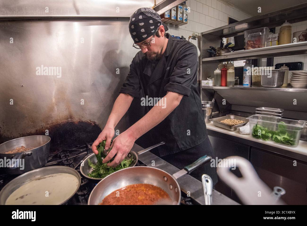 19 dicembre 2017 - Baltimora, Maryland, Stati Uniti - lo chef maschile mette gli spinaci selvaggi in padella in una cucina commerciale a Baltimora, MD (immagine di credito: © Edwin Remsberg / Vwpics/VW Pics via ZUMA Wire) Foto Stock
